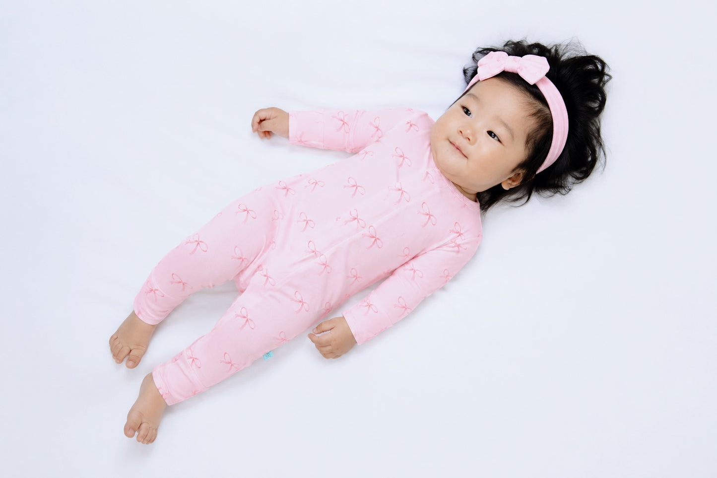 Baby in a pink outfit with pink bows lying on a white background